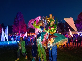 lichternacht-im-kurpark-2 Zwei fantasievoll kostümierte Künstler auf Stelzen, beleuchtet von strahlenden Lichtern; im Hintergrund genießt eine bunte Menge die festliche Abendstimmung im Kurpark.Two imaginatively costumed artists on stilts, illuminated by shining lights; in the background, a colorful crowd enjoys the festive evening atmosphere in the spa gardens.To fantasifuldt udklædte kunstnere på stylter, oplyst af skinnende lys; i baggrunden nyder en farverig menneskemængde den festlige aftenstemning i spa-haven.Twee fantasierijk gekostumeerde artiesten op stelten, verlicht door stralende lampjes; op de achtergrond geniet een kleurrijk publiek van de feestelijke avondsfeer in de tuinen van het kuuroord.