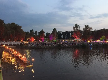 fackelschwimmen Fackelschwimmen bei der Dämmerung: Menschenmengen säumen das Ufer, während glühende Fackeln auf dem Wasser treiben und eine festliche Atmosphäre entsteht.