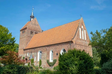 kirchenführung Historische Backsteinkirche mit markantem Kirchturm und rotem Ziegeldach, umgeben von grüner Natur.