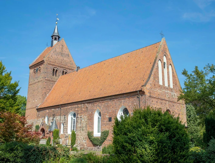 kirchenführung Historische Backsteinkirche mit markantem Kirchturm und rotem Ziegeldach, umgeben von grüner Natur.