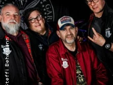 Vier Männer in Freizeitkleidung, fröhlich posierend vor einem schwarzen Hintergrund.