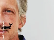 Ein Mann mit silbergrauem Haar und Bart in Nahaufnahme vor weißem Hintergrund.