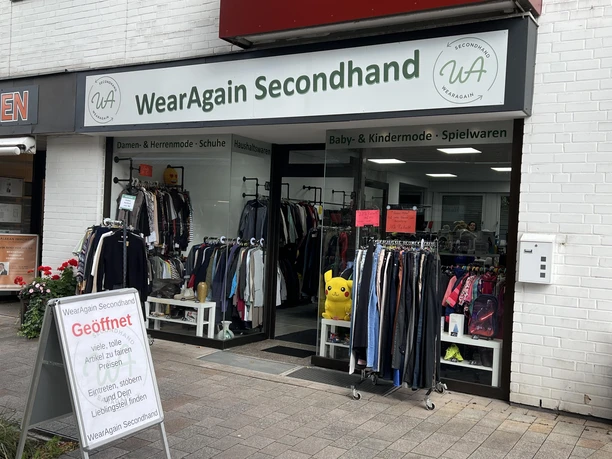 Eingang von WearAgain Secondhand mit Kleiderständern und Werbetafel vor dem Laden