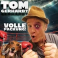 Comedian Tom Gerhardt posiert in Boxpose, ein Hund trägt rote Boxhandschuhe, im Hintergrund der Boxring.