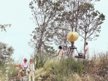 Eine Gruppe von Personen steht auf einem bewachsenen Hügel neben einem gelben Kunstwerk.