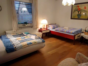 Haus am Park 2 (C) Gaby Schramm.jpg Gemütliches Schlafzimmer mit zwei Betten, einem Fenster, hölzernem Boden und ruhiger Beleuchtung.