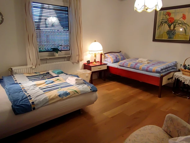 Haus am Park 2 (C) Gaby Schramm.jpg Gemütliches Schlafzimmer mit zwei Betten, einem Fenster, hölzernem Boden und ruhiger Beleuchtung.