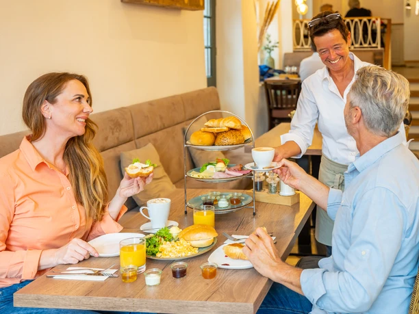 Frühstück im Cafe Bös, Ratingen Ein entspanntes Frühstückserlebnis im Café, zwei Gäste genießen Brötchen und Kaffee mit fröhlicher Bedienung.