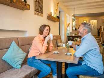 Café Bös, Ratingen Zwei Personen unterhalten sich bei einer Tasse Kaffee in einem hellen, einladenden Café mit Holzmöbeln.