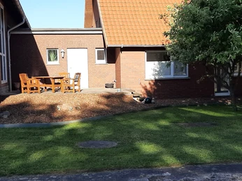 20240515_075410.jpg Ein rotes Ziegelgebäude mit Spitzdach, Gartenmöbeln auf der Terrasse und einem gepflegten Rasen.