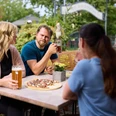Restaurant Zur Post <p>Vier Personen genießen Getränke und Pizza in einem sonnigen Biergarten, umgeben von grüner Natur.</p>