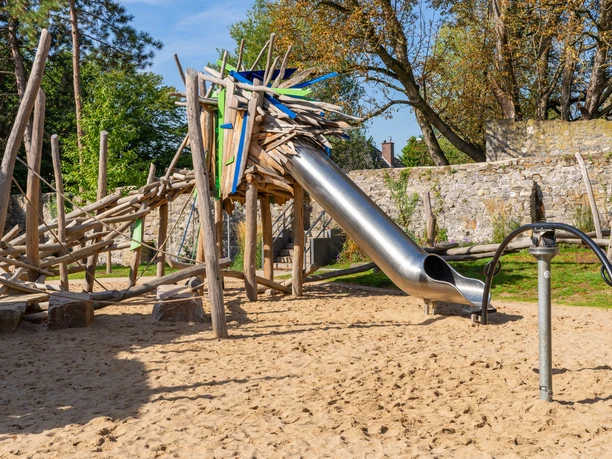Drachenspielplatz Ratingen Ein Abenteuerspielplatz mit Holzstruktur und Rutsche lädt in einer naturnahen Umgebung zum Spielen ein.
