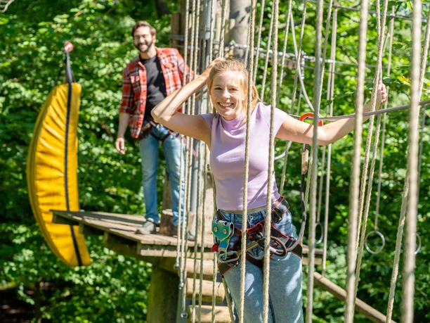 Hängebrücke im Waldkletterpark Velbert Junge Frau und Mann mit Klettergurten auf der Hängebrücke im dichten Grün des Waldkletterparks Velbert.