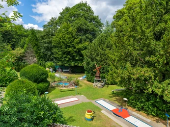 Minigolf Anlage in Velbert Minigolfanlage in Velbert mit abwechslungsreichen Bahnen, umgeben von dichten grünen Bäumen.