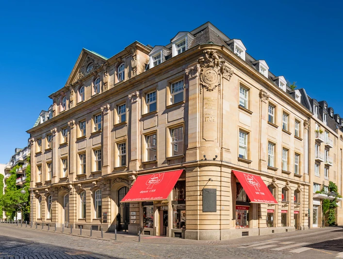 Farina Fragrance Museum Das Farina-Haus in Köln zeigt eine historische Fassade mit klassischer Architektur und rot-weißen Markisen vor einem klaren blauen Himmel.The Farina House in Cologne features a historic façade with classic architecture and red and white awnings against a clear blue sky.
