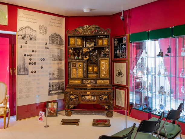 Farina Fragrance Museum An opulently decorated room in the Farina Fragrance Museum shows a richly decorated baroque cabinet with colorful perfume bottles in a glass display case, brightly lit and framed by red walls.