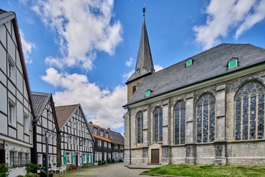Historischer Ortskern mit Kirchplatz in Wülfrath Kirchplatz in Wülfrath mit beeindruckender Kirche und traditionellen Fachwerkhäusern unter blauem Himmel.