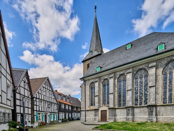 Historischer Ortskern mit Kirchplatz in Wülfrath Kirchplatz in Wülfrath mit beeindruckender Kirche und traditionellen Fachwerkhäusern unter blauem Himmel.