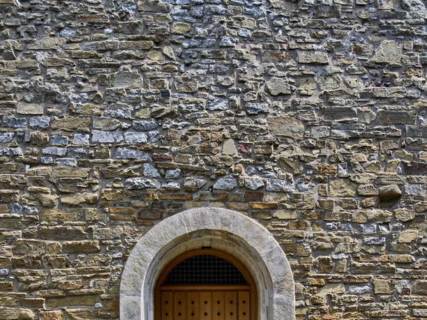 Historischer Ortskern Wülfrath Kirchplatz Hölzerne Tür in einem mittelalterlichen Steinbogen, umgeben von massivem Mauerwerk und Pflastersteinen.