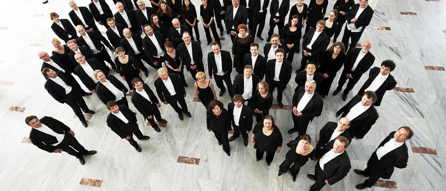 NWD_2_Foto_Joachim_Grothus.jpg Eine große Gruppe von Musikern in formeller Kleidung steht in einer weißen Halle und blickt nach oben.