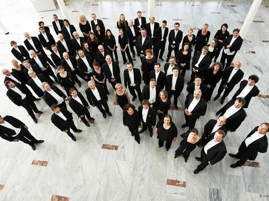 NWD_2_Foto_Joachim_Grothus.jpg Eine große Gruppe von Musikern in formeller Kleidung steht in einer weißen Halle und blickt nach oben.