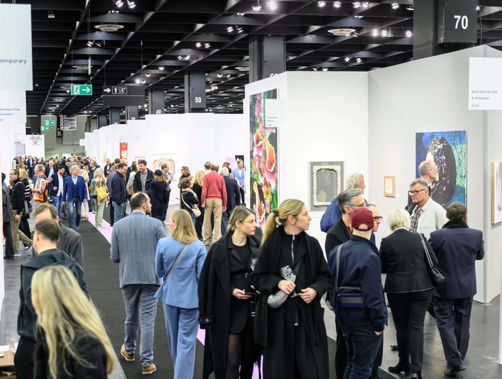 ART COLOGNE Menschen flanieren entlang der Stände, betrachten aufmerksam verschiedene Kunstwerke, die an weißen Wänden präsentiert werden. Im Vordergrund zieht eine bunte Mischung aus Gemälden die Blicke der Betrachter*innen auf sich, während die Decke durch industrielle Beleuchtung hervorsticht. Die Szene wirkt lebendig und zeigt das Interesse der Menschen an zeitgenössischer Kunst.People stroll along the stands, attentively looking at various works of art presented on white walls. In the foreground, a colorful mixture of paintings catches the viewer's eye, while the ceiling stands out with industrial lighting. The scene looks lively and shows people's interest in contemporary art.