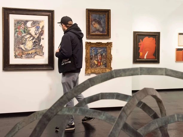 ART COLOGNE A visitor looks at works in a gallery. Works of art are displayed on white walls.