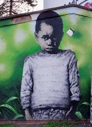 Mural Ein großformatiges Graffiti zeigt einen jungen Jungen mit ernstem Blick vor einem grünen Hintergrund. Auf seinem Pullover steht die verblasste Botschaft: „I WILL NEVER SAY WHAT YOU WANT TO HEAR“.