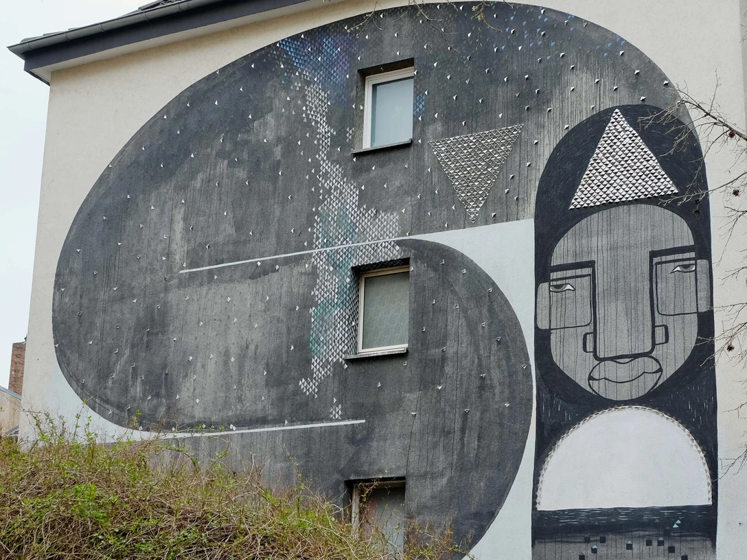 Mural Das beeindruckende Wandgemälde auf dem Gebäude zeigt abstrahierte Formen und Gesichter in Schwarz-Weiß-Tönen.The impressive mural on the building shows abstract shapes and faces in black and white tones.