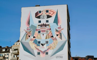 Mural Das Bild zeigt ein beeindruckendes Wandgemälde in Köln. Es stellt ein stilisiertes Wolfsdesign dar, das in einer modernen, geometrischen Art gestaltet ist. Die verwendeten Farben und Formen erzeugen einen dynamischen und urbanen Look, der die Kreativität und Vielfalt der Stadt widerspiegelt.