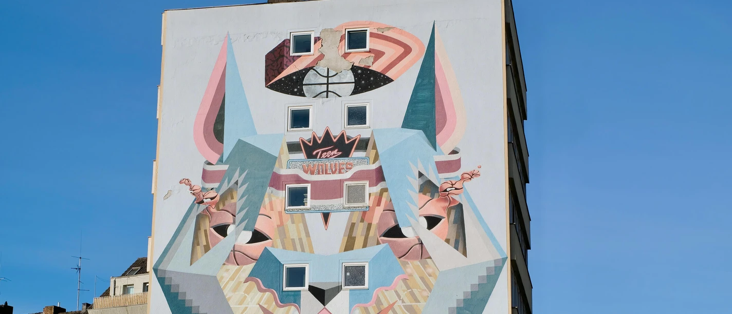 Mural The picture shows an impressive mural in Cologne. It depicts a stylized wolf design created in a modern, geometric style. The colors and shapes used create a dynamic and urban look that reflects the creativity and diversity of the city.