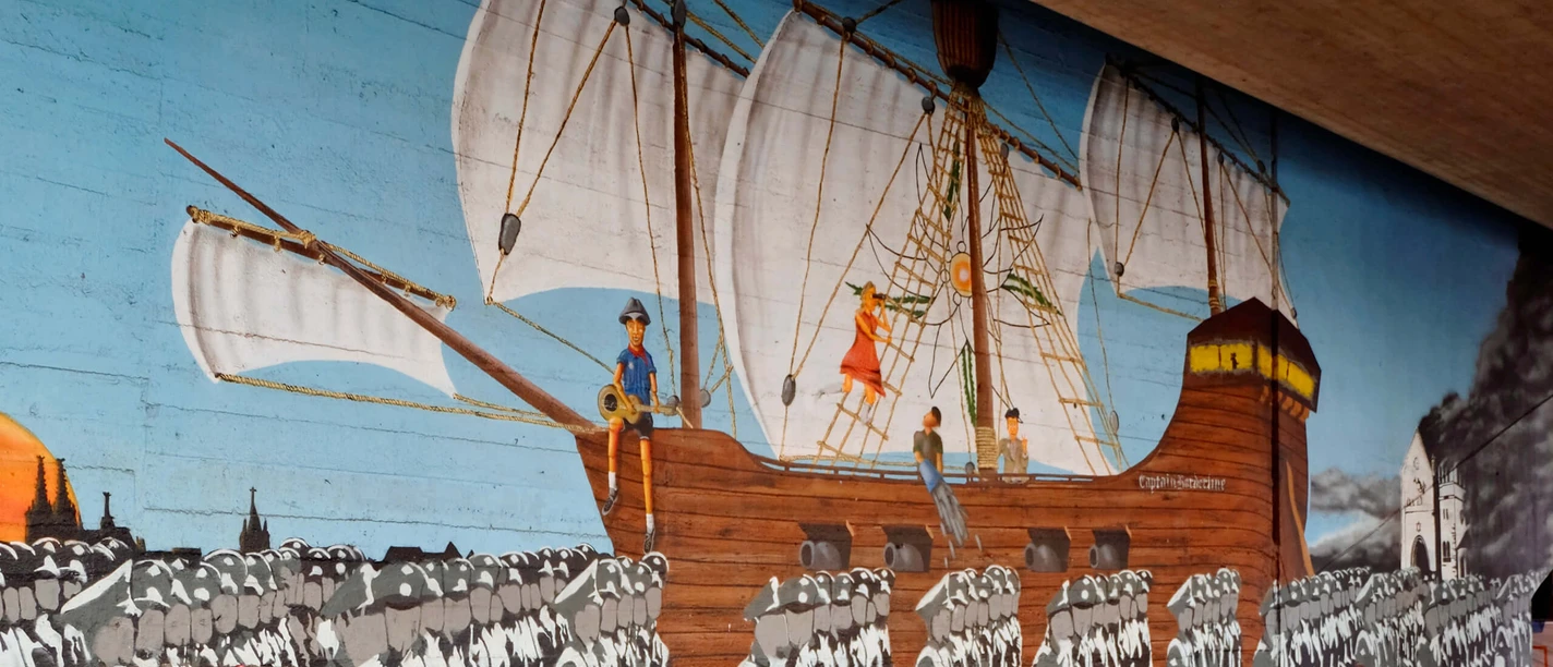 Mural Ein großflächiges Wandgemälde zeigt eine historische Szene der Edelweißpiraten in Köln. Ein Segelschiff mit weißen Segeln zieht über den Ozean, während im Vordergrund eine marschierende Menschenmenge zu sehen ist. Am linken Bildrand ist ein Porträt eines jungen Mannes zu erkennen. Das lebendige, historische Kunstwerk ziert eine Unterführung und erinnert an die soziale Geschichte der Stadt.