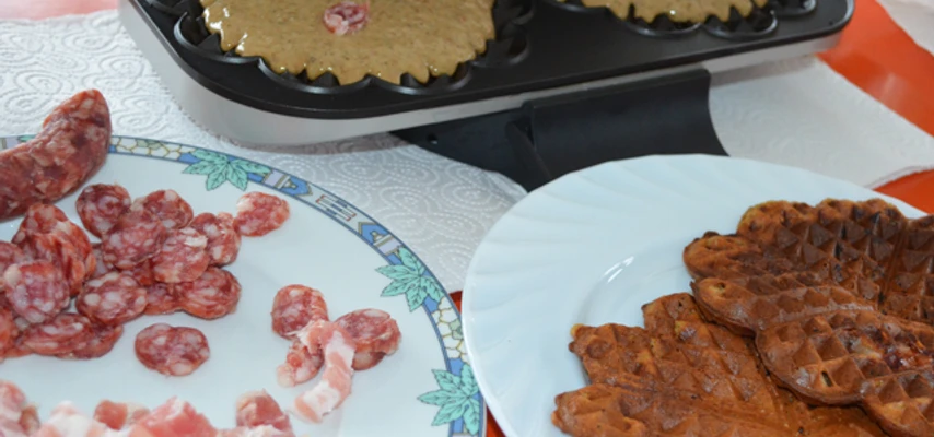 Speckendicken zu Silvester Geöffnetes Waffeleisen mit Teig und Speckstücken, daneben Teller mit Salami, Speck und fertigen Waffeln.