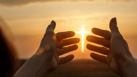 Bethaus Das Bild zeigt einen Sonnenuntergang im Hintergrund. Zwei Hände werden hochgehalten, und zwischen ihnen ist das Jesuskreuz zu sehen, das die Sonne darstellt.