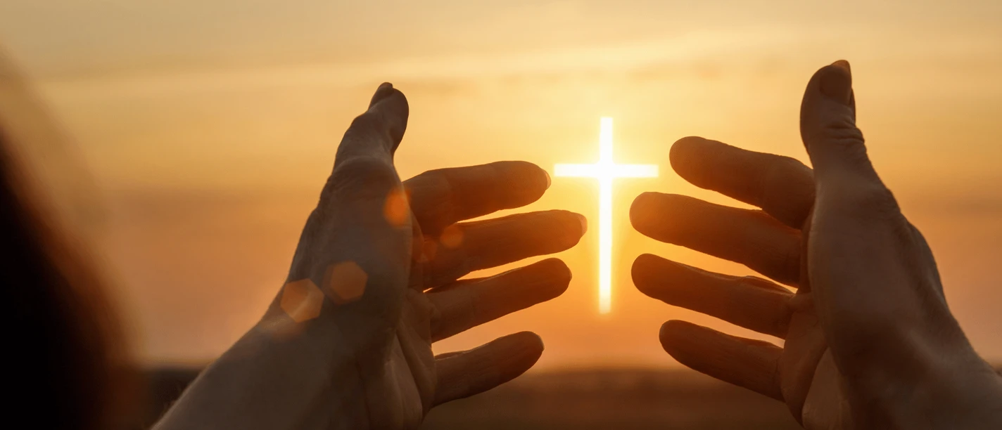 Bethaus Das Bild zeigt einen Sonnenuntergang im Hintergrund. Zwei Hände werden hochgehalten, und zwischen ihnen ist das Jesuskreuz zu sehen, das die Sonne darstellt.