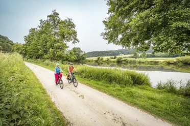 Am Fünf-Flüsse-Radweg bei Krachenhausen Zwei Radfahrer auf einem geschotterten Abschnitt des Fünf-Flüsse-Radwegs fahren entlang der Naab bei Krachenhausen