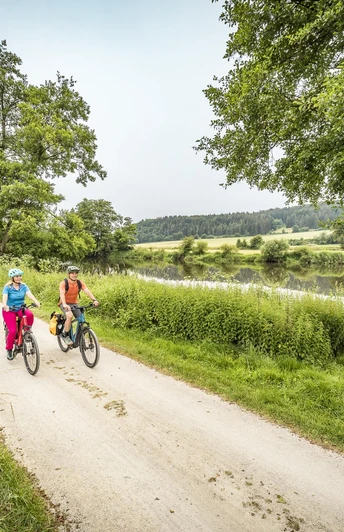 Am Fünf-Flüsse-Radweg bei Krachenhausen Zwei Radfahrer auf einem geschotterten Abschnitt des Fünf-Flüsse-Radwegs fahren entlang der Naab bei Krachenhausen