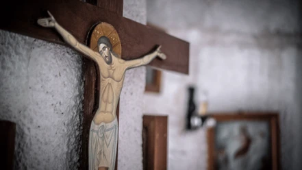 Evangelische Kirche Eidinghausen Destination one.png Kruzifix aus Holz mit Jesus-Figur, Hintergrund wirkt rustikal mit einem verschwommenen Bildrahmen.
