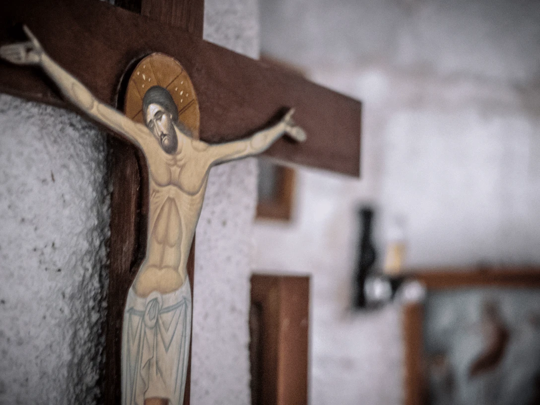 Evangelische Kirche Eidinghausen Destination one.png Kruzifix aus Holz mit Jesus-Figur, Hintergrund wirkt rustikal mit einem verschwommenen Bildrahmen.
