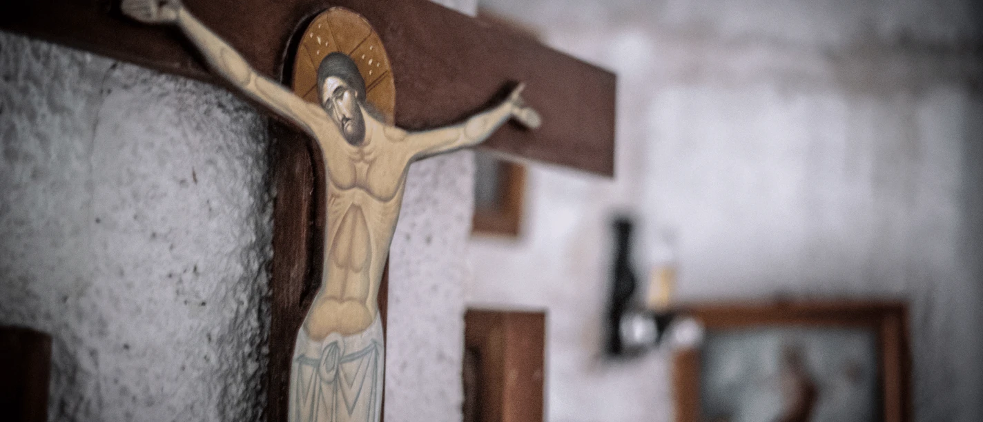 Evangelische Kirche Eidinghausen Destination one.png Kruzifix aus Holz mit Jesus-Figur, Hintergrund wirkt rustikal mit einem verschwommenen Bildrahmen.