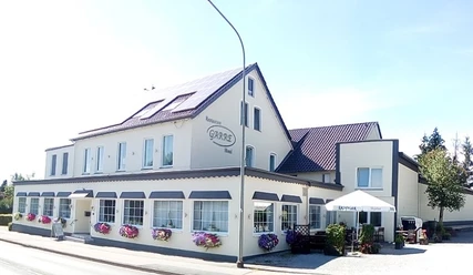IMG_20200730_152409.jpg Ein zweistöckiges Restaurant mit hellen Wänden, Fenstern in Reih und Solarzellen auf dem Dach.