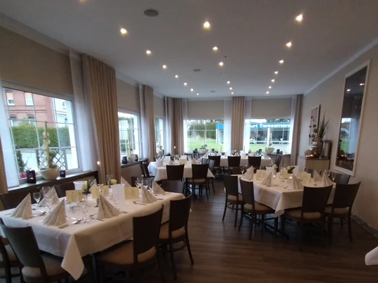 IMG_20200118_110013M2P.jpg Festlich eingedeckter Speisesaal mit weiß gedeckten Tischen und gedeckter Beleuchtung, große Fenster.