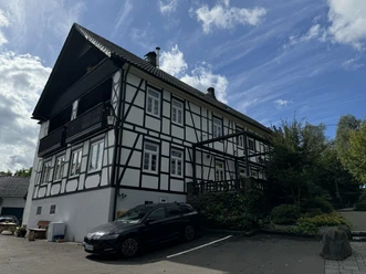 In der Delling Fachwerkhaus mit schwarzen Holzbalken, weißen Wänden und gepflegtem Garten unter einem blauen Himmel.