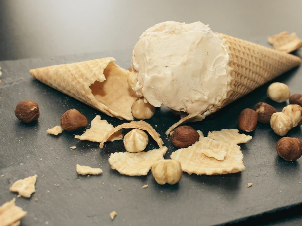 Gottschalk's Hof Haselnusseis Haselnusseis serviert in zerbrochener Waffel auf Schieferplatte, umgeben von ganzen Haselnüssen.
