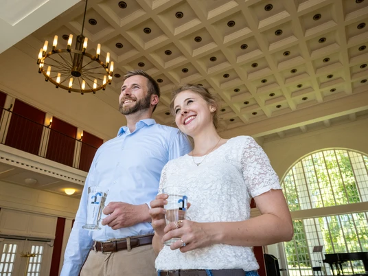 Heilwasser in der Wandelhalle Das Bild zeigt einen Mann und eine Frau in der Wandelhalle, die gerade das Heilwasser aus Bad Oeynhausen in Gläsern trinken. Beide sehen zufrieden aus und lächeln.