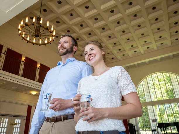 Heilwasser in der Wandelhalle Das Bild zeigt einen Mann und eine Frau in der Wandelhalle, die gerade das Heilwasser aus Bad Oeynhausen in Gläsern trinken. Beide sehen zufrieden aus und lächeln.