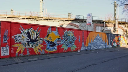 Mural Eine lange, leuchtend rote Mauer am Straßenzug ist mit bunten, abstrakten Kunstwerken verziert.