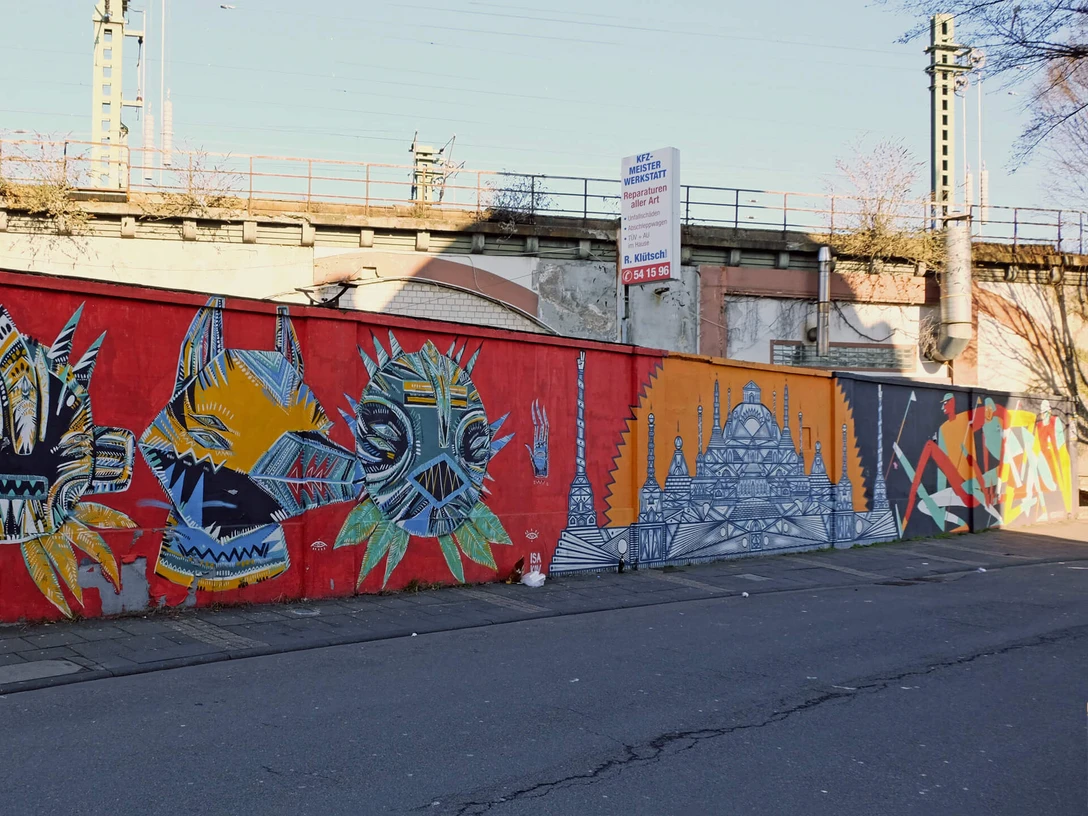 Mural Eine lange, leuchtend rote Mauer am Straßenzug ist mit bunten, abstrakten Kunstwerken verziert.A long, bright red wall along the street is decorated with colorful, abstract works of art.