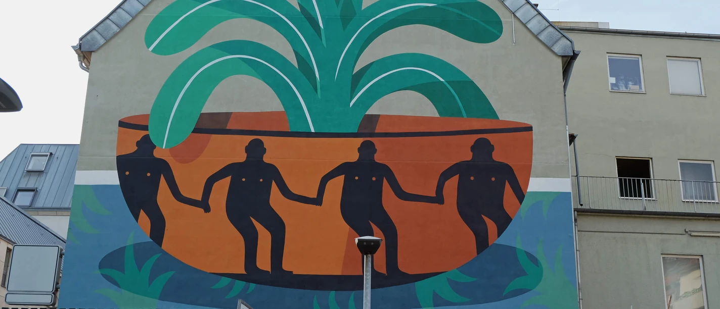 Mural Das Wandgemälde auf einer Hauswand zeigt vier figürlich stilisierte Personen in einer großen, pflanzenähnlichen Schale, umgeben von grünen und orangefarbenen Formen.