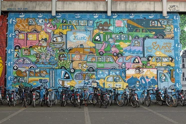 Mural Buntes Mural mit vielen fröhlich gezeichneten Autos, darunter parkende Fahrräder.
